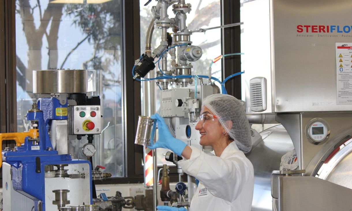 Researcher in food lab, dressed in lab coat and holding metal can