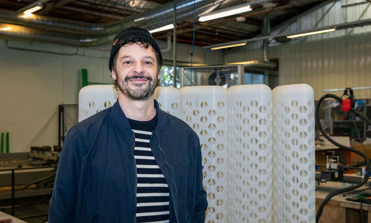 Dr Olivier Cotsaftis smiling as he stands in front of his 3D printed furniture. 