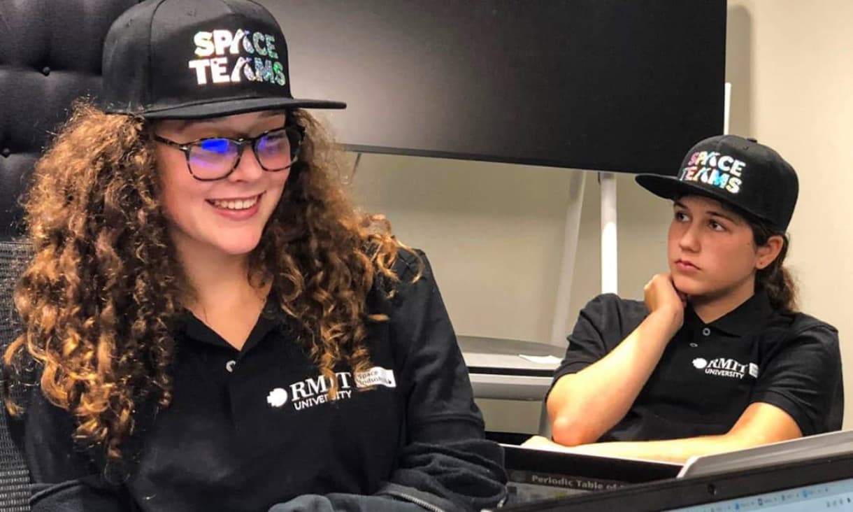two people sitting at a desk with hats on that say Space Teams
