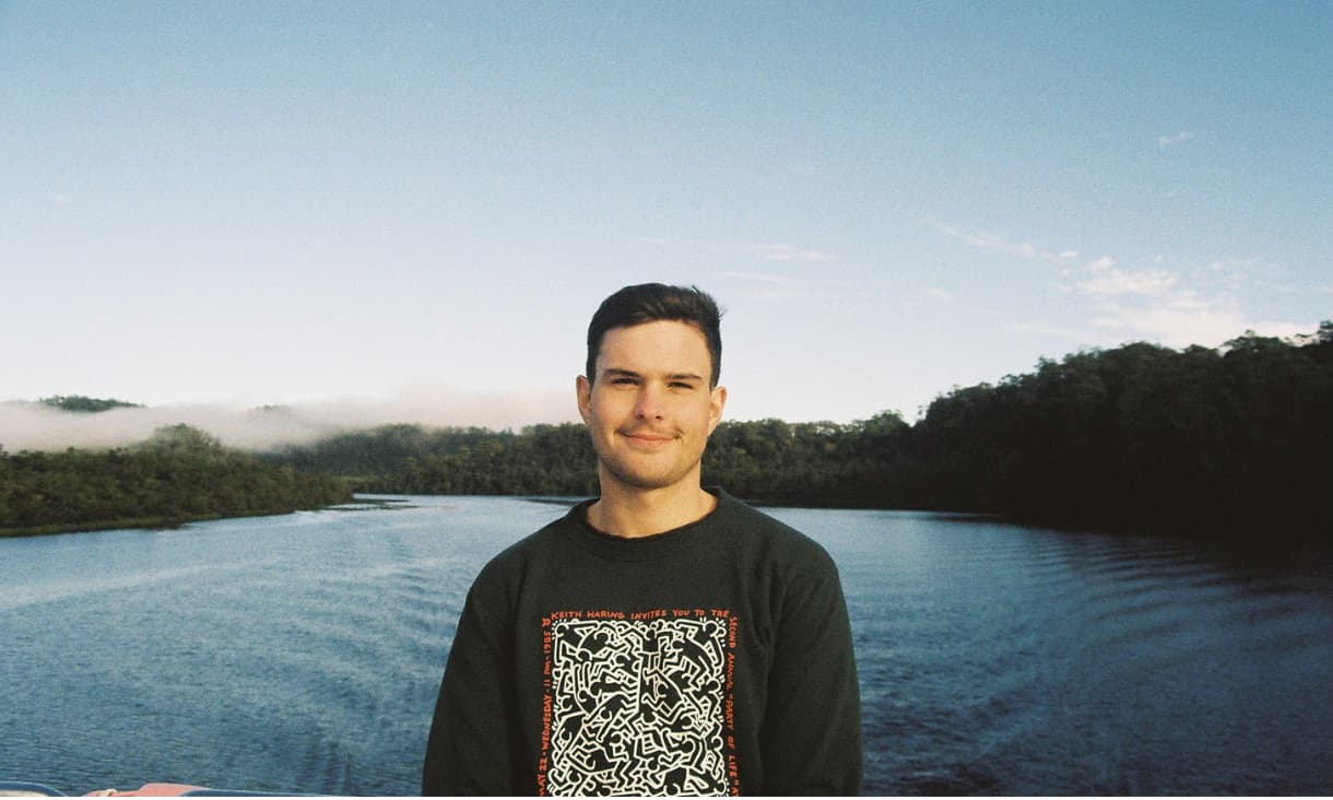 Blake Hillebrand standing in front of a body of water with trees in the distance