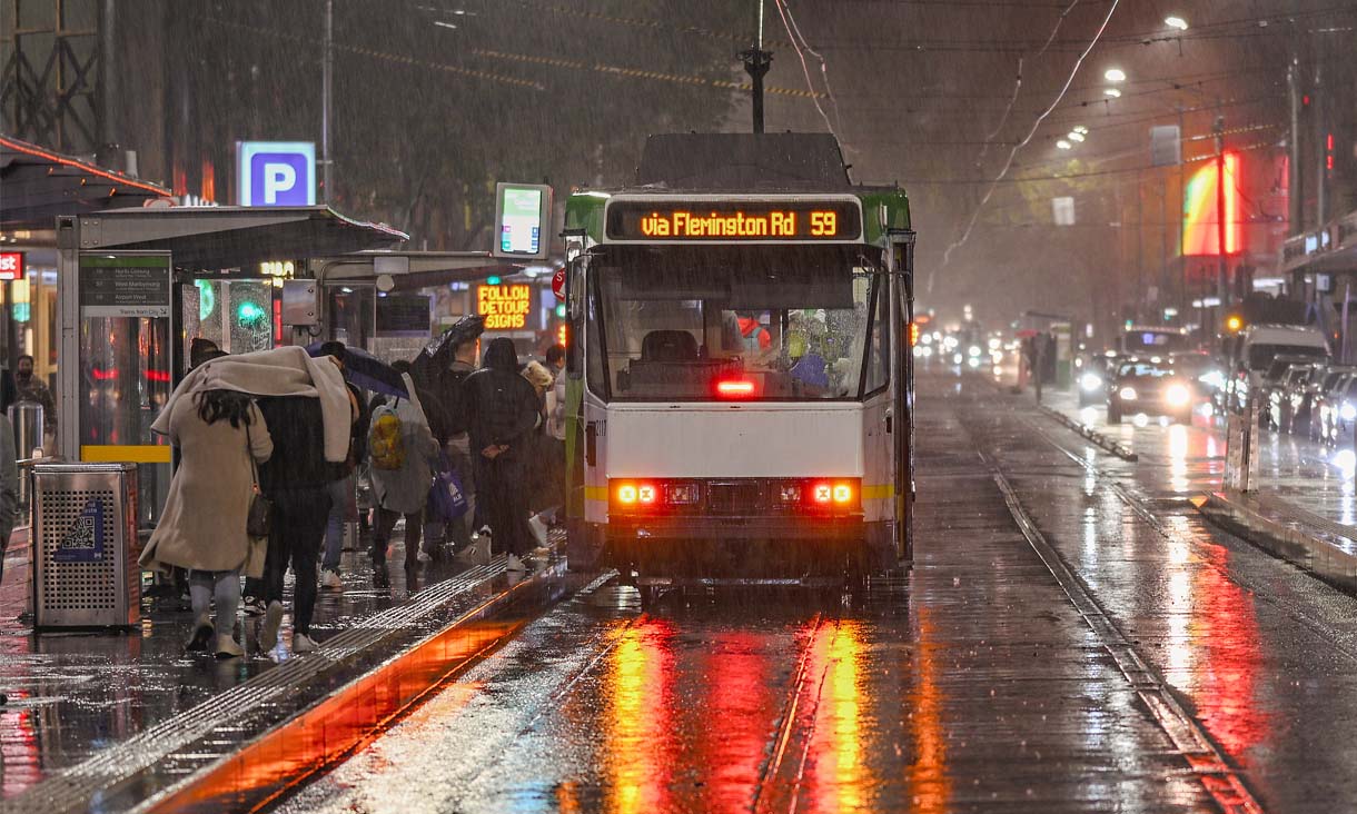 People running in the rain trying to hop on a tram.