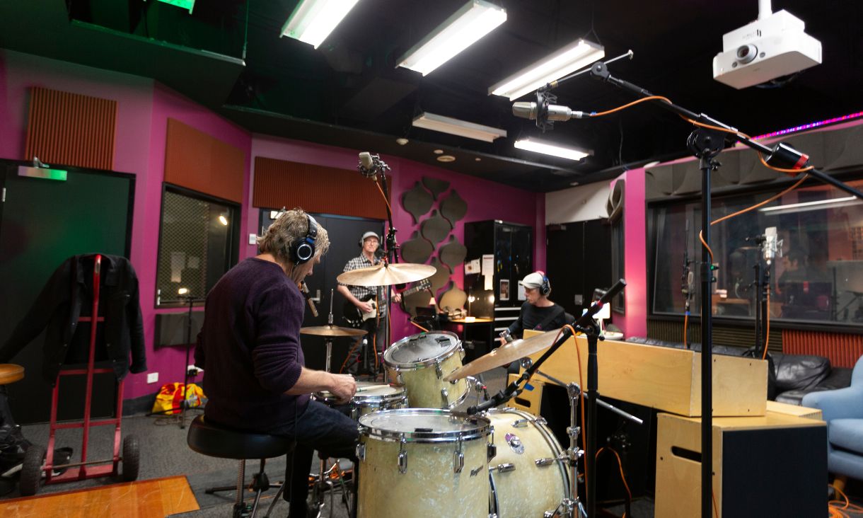 Three members of band Models recording in studio, one on drums, the other two on guitar