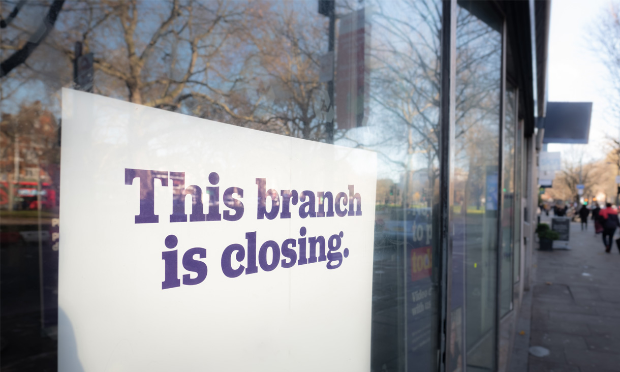 A poster on the window of a bank reads "this bank is closing"