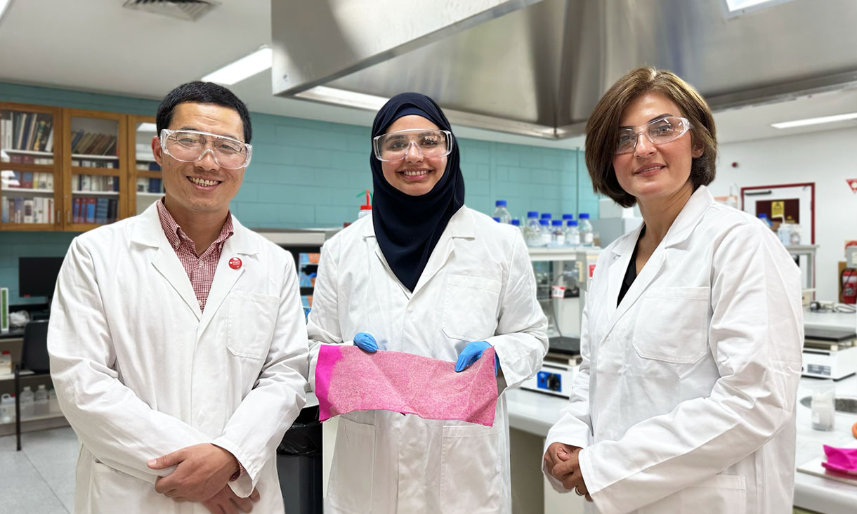 From left to right: Research supervisor and RMIT Senior lecturer Dr Xin Wang, Lead researcher and RMIT research assistant Dr Aisha Rehman and Project leader and RMIT Senior Lecturer Dr Shadi Houshyar. Aisha is holding pink cotton that’s been treated with nanodiamonds. Everyone is wearing white lab coats and protective goggles.