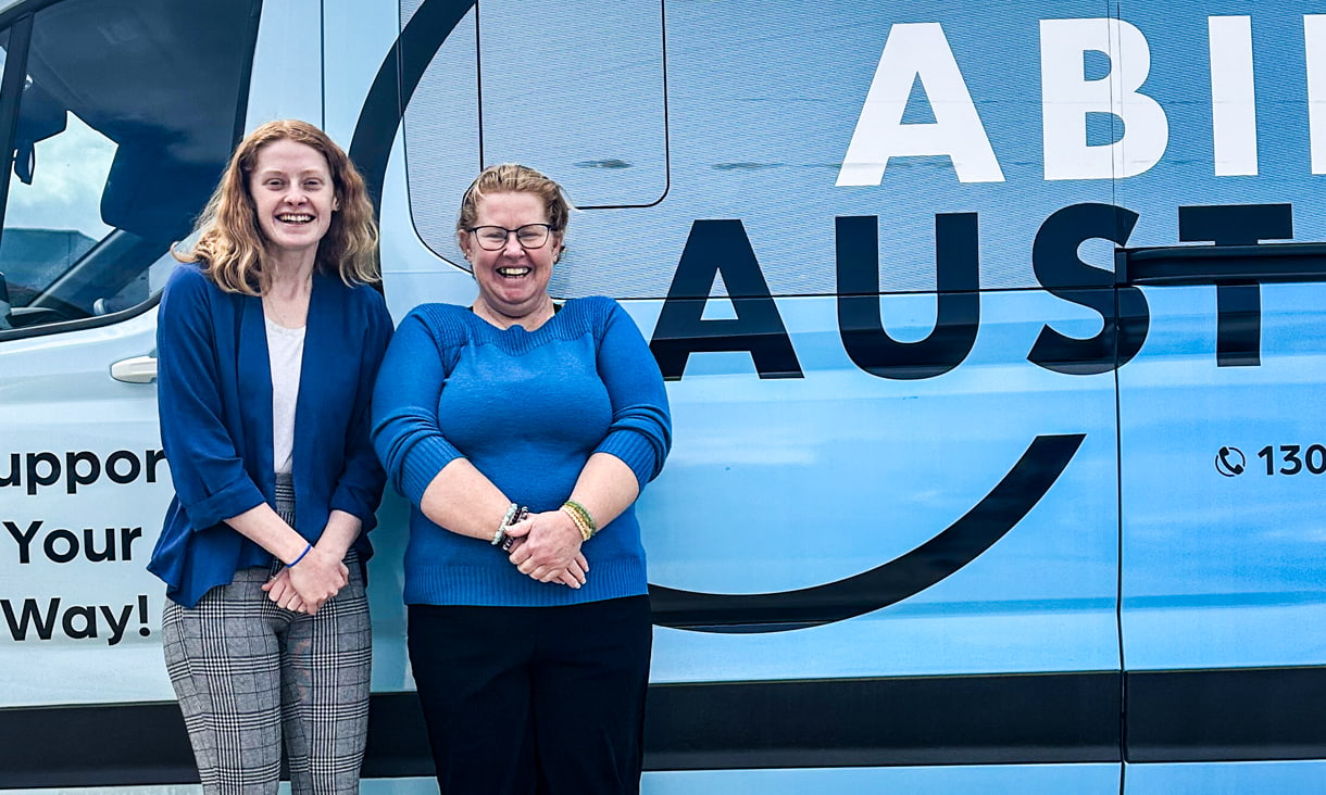 2 women stand in front of a blue van.