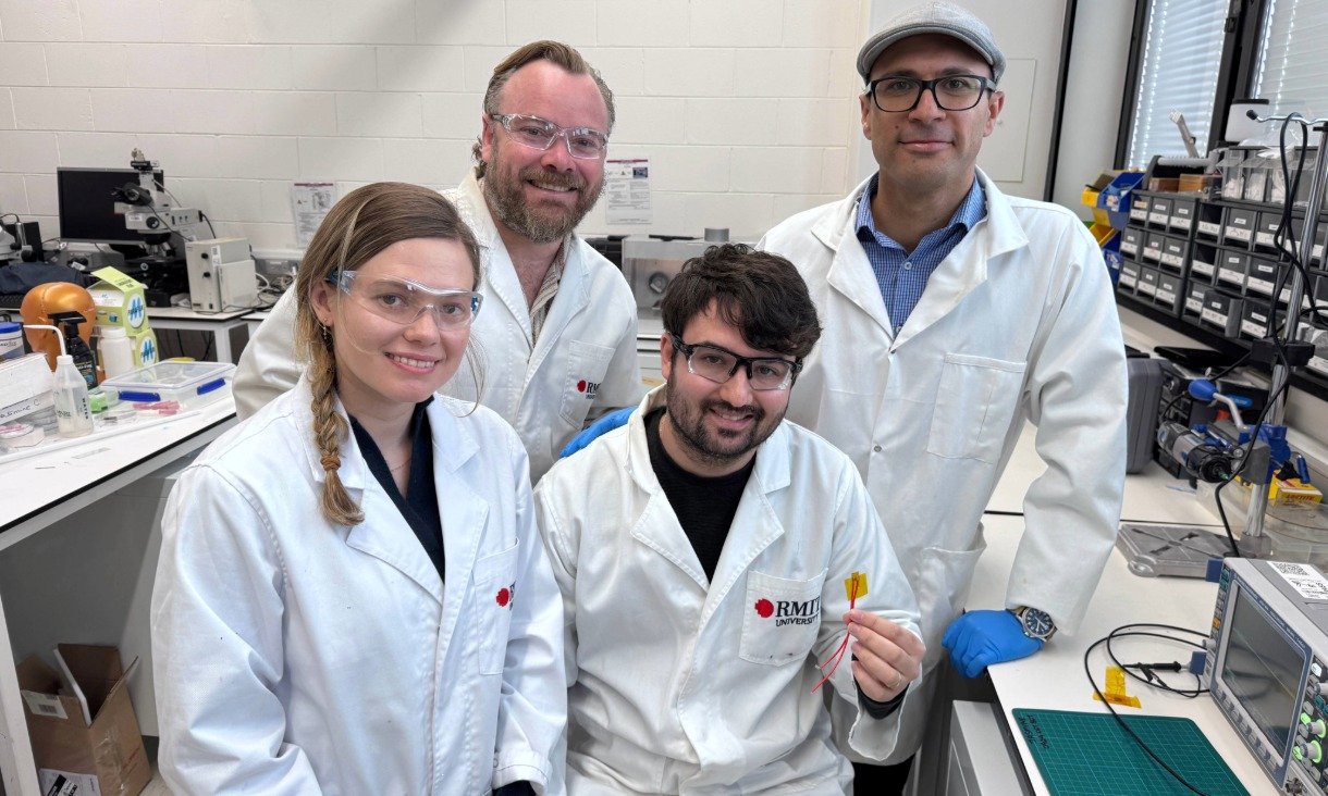 A group of four researchers in lab coats stand together in a laboratory; one holds a small nylon‑film device used in the team’s energy‑harvesting study.