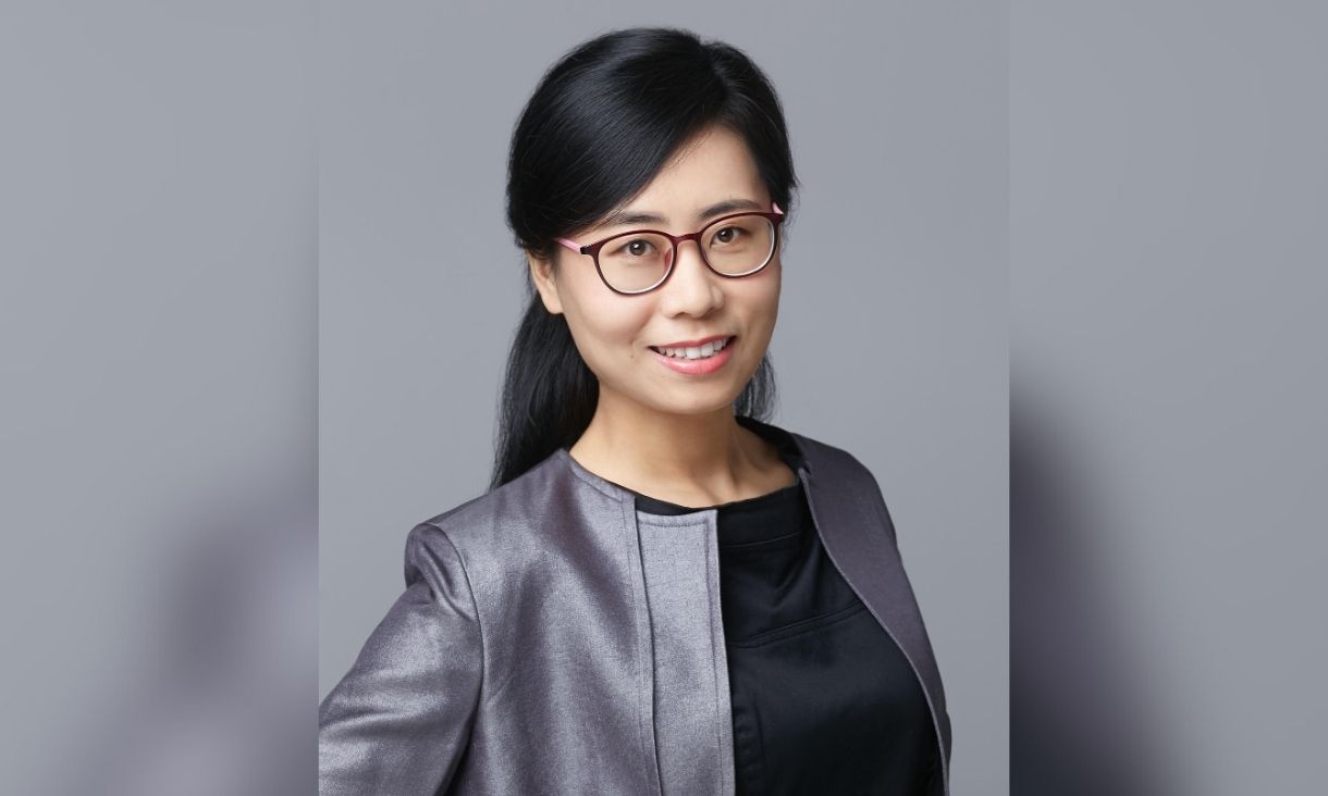 Dr Nancy An poses in front of a grey background, wearing a dark grey outfit. She is smiling.