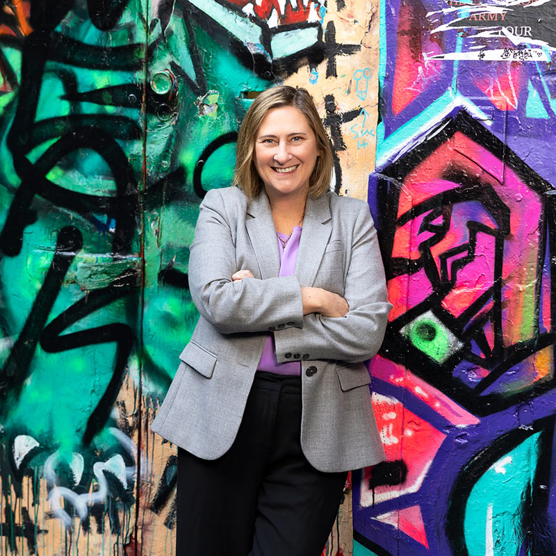 A portrait of Kathy Douglas in a city laneway with graffiti artwork behind her
