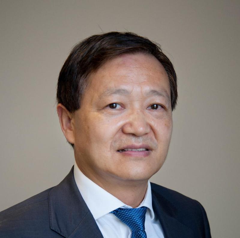 Profile photo of Professor Chun-Qing Li. Professor Li is standing in front of a brown wall, standing at an angle and smiling at camera. Professor Li is wearing a white collared shirt, blue tie and black blazer.