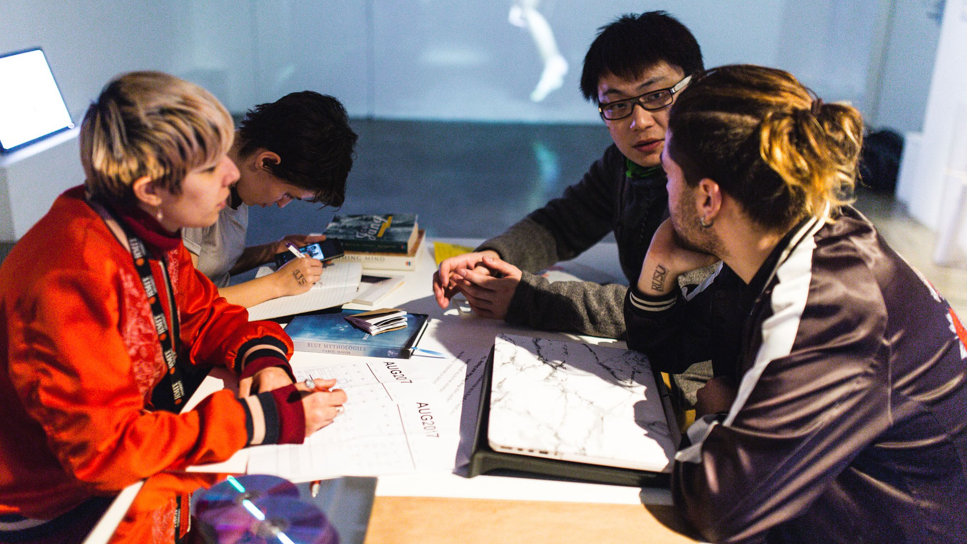 Four students sitting opposite each other , discussing a project and taking notes