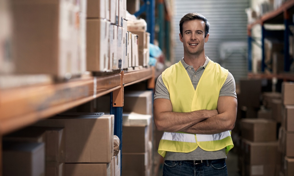 Supply chain professional wearing safety vest with arms crossed in warehouse