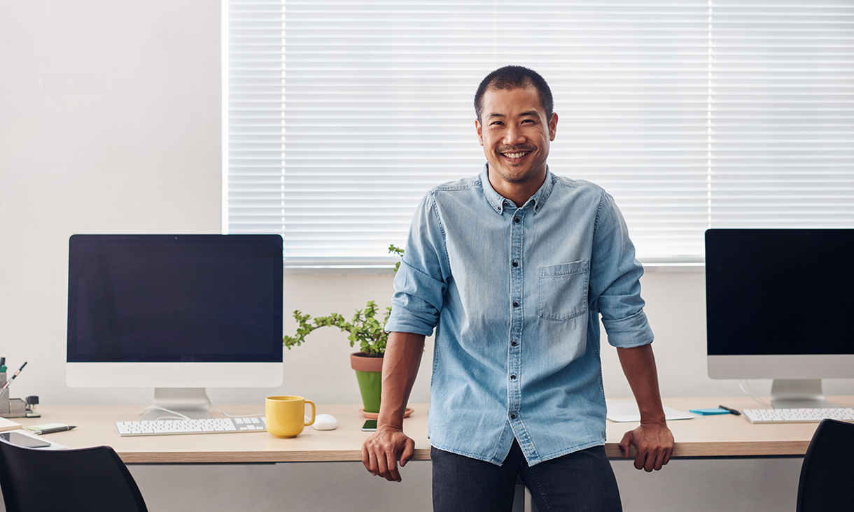 Male professional leaning on desk while smiling